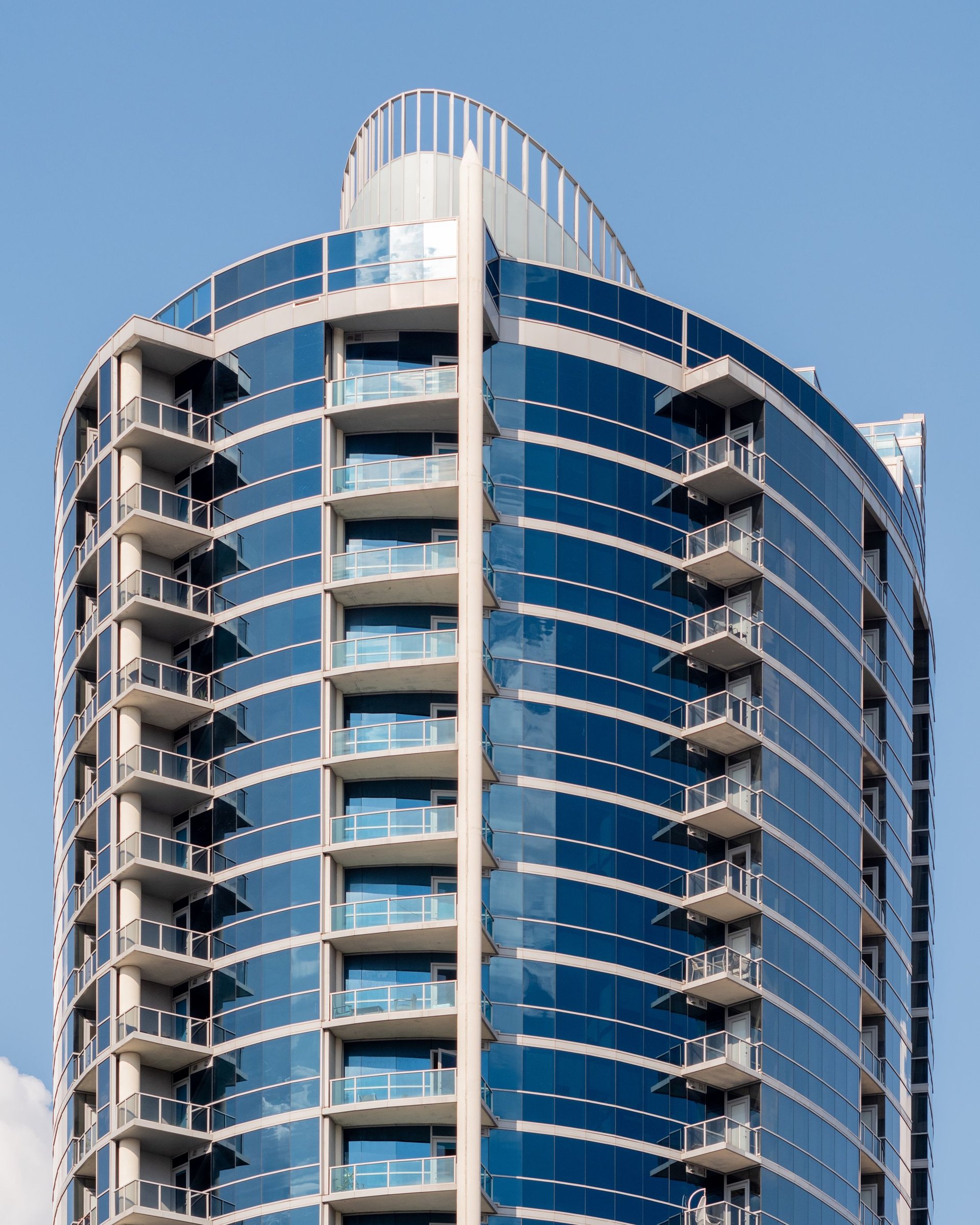 Curved residential tower with glass balconies under a blue sky